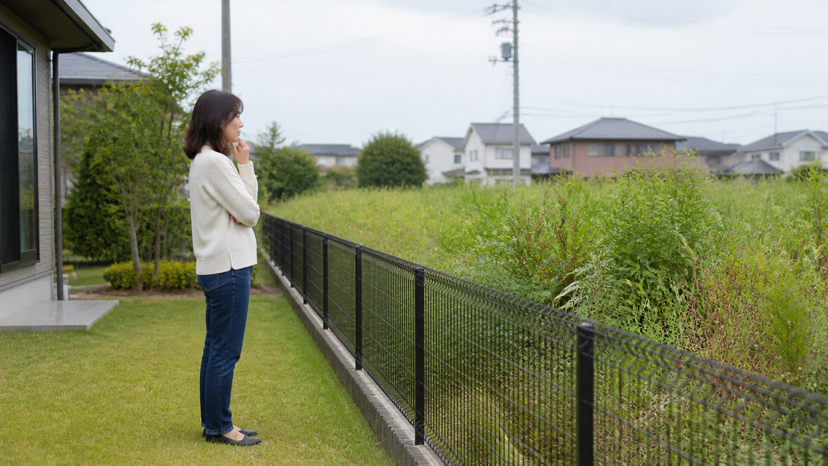 隣の雑草だらけの空き地を自宅側から確認する人